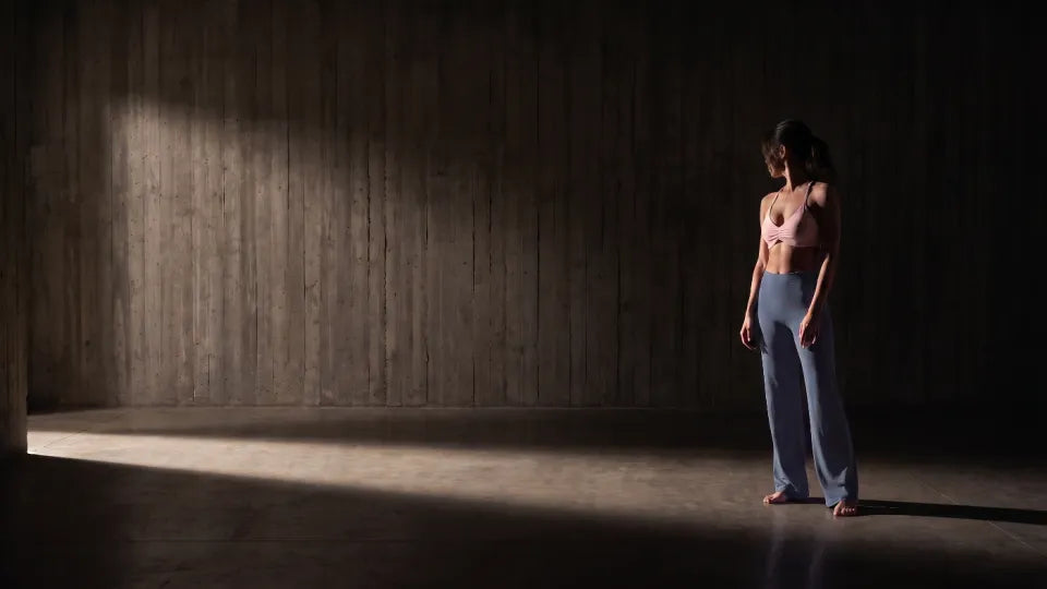 Salle de béton, lumière rasante — La Brassière Nouée rose poudré et Le Pantalon Droit bleu-gris.